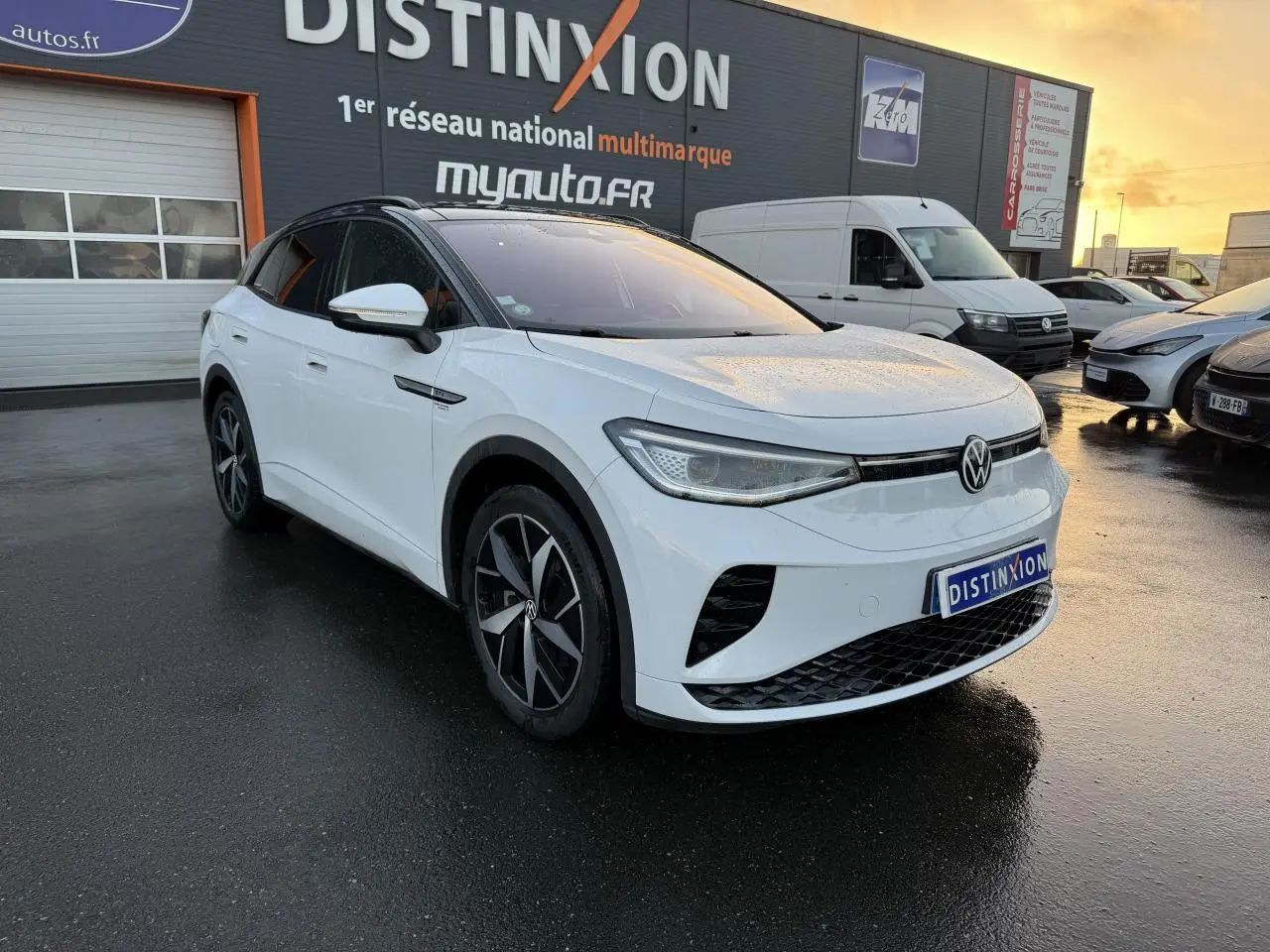 Volkswagen ID.4 GTX blanc glacier en 3/4 avant droit, toit noir et jantes bi-colores, stationné devant un garage