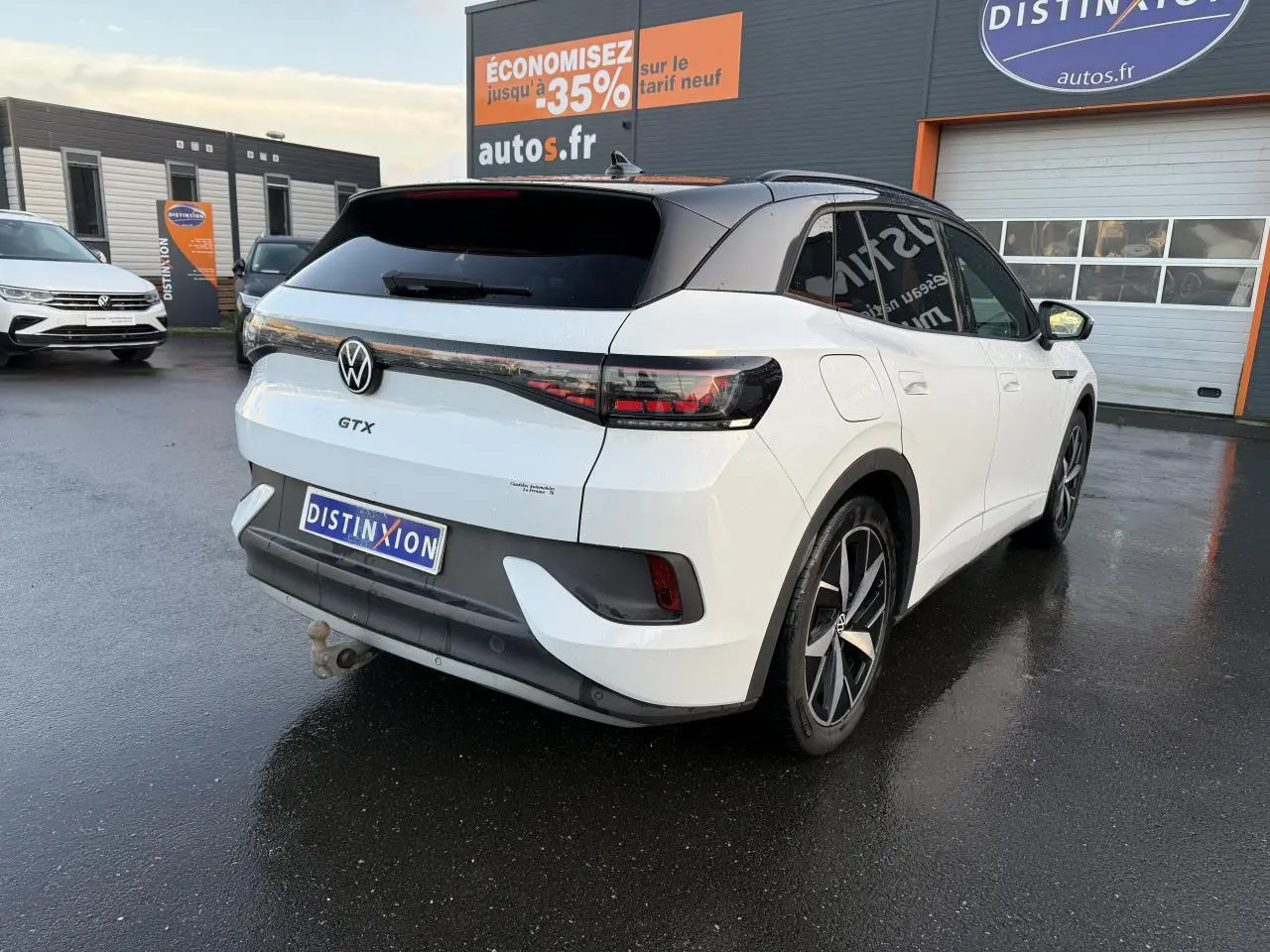 Vue 3/4 arrière droite d'un Volkswagen ID.4 GTX blanc glacier métallisé avec toit noir et crochet d'attelage.