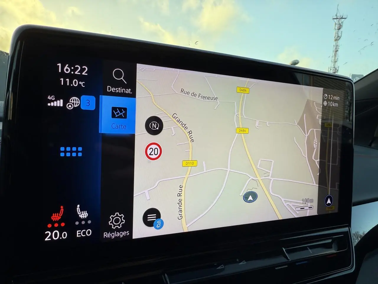 Vue intérieure du tableau de bord du Volkswagen ID.4 GTX blanc, écran tactile affichant la navigation et la température à 20°C.