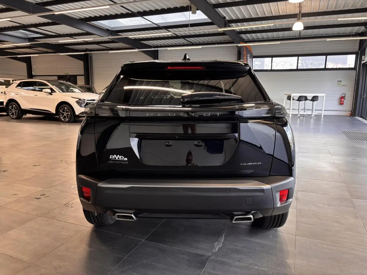 Vue arrière d'un Peugeot 2008 noir hybride 2025 en showroom avec double sortie d'échappement chromée.