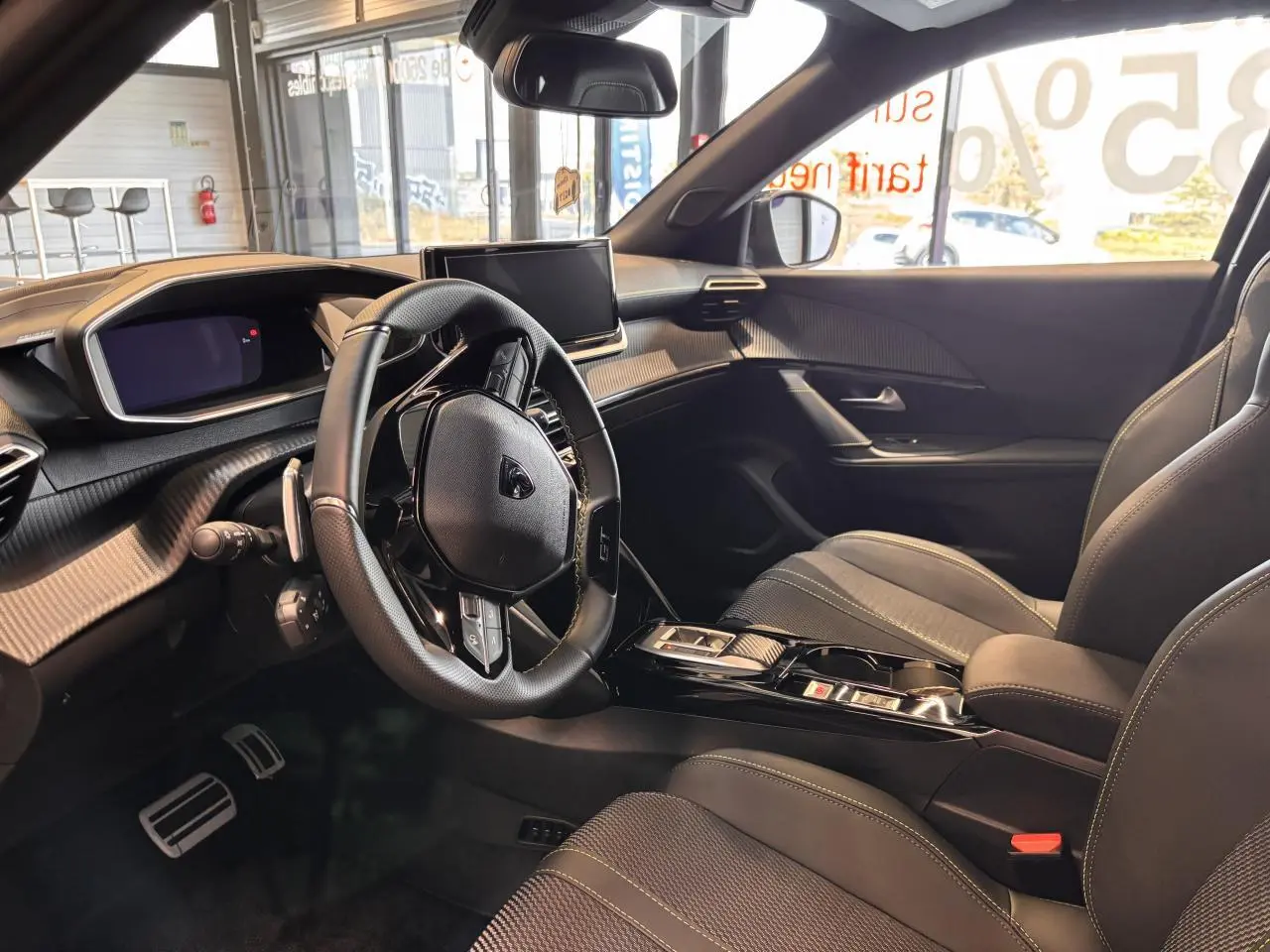 Intérieur avant droit du Peugeot 2008 GT 2025 avec volant compact cuir, écran tactile et sellerie tissu noire surpiquée.