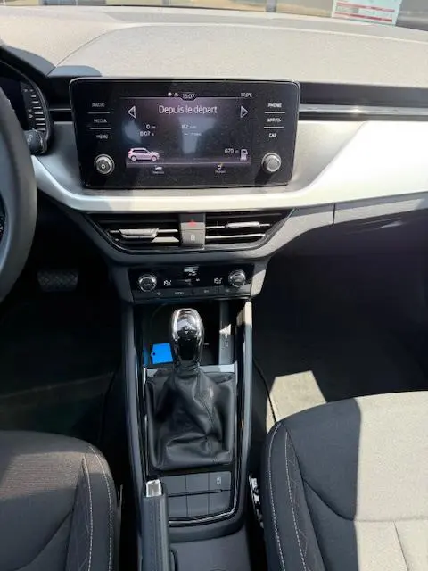 Vue intérieure centrée sur la console centrale et l'écran tactile du Skoda Kamiq noir, avec levier de vitesse automatique.