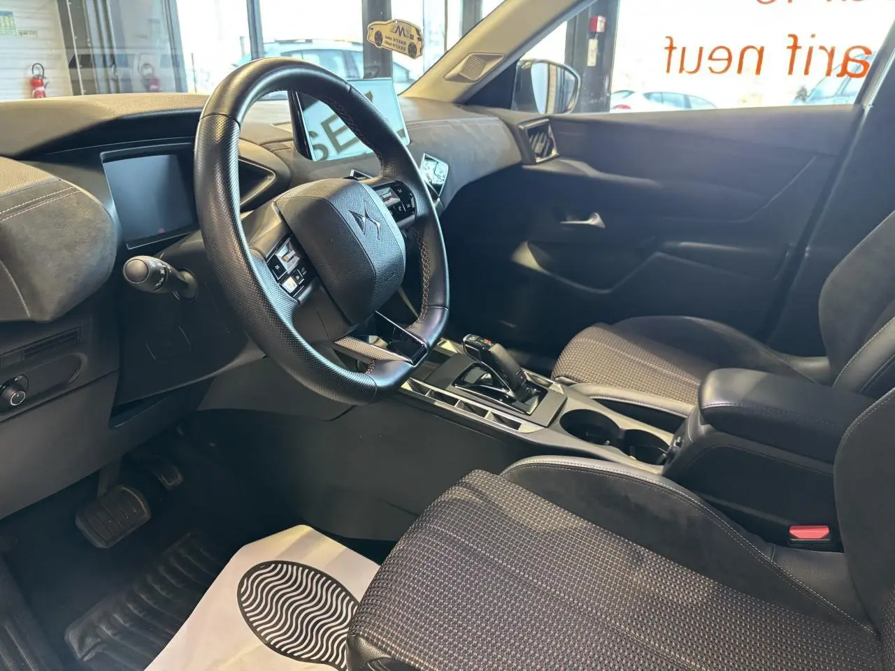 Vue intérieure côté conducteur du DS3 Crossback 2024 en Crystal Pearl, montrant le volant, la console centrale et les sièges noirs.