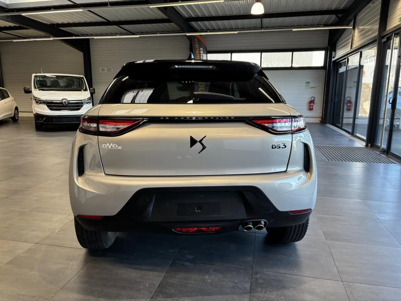 Vue arrière d'un DS3 Crossback 2024 Crystal Pearl avec double sortie d'échappement, en intérieur de showroom.