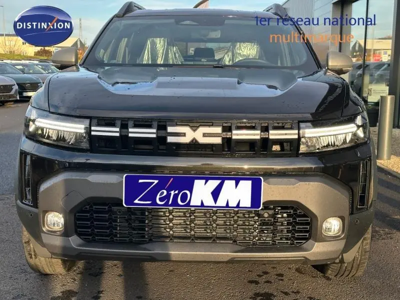 Vue frontale d'un Dacia Duster 1.8 hybrid 155ch Journey noir nacré métallisé avec calandre distinctive et phares LED allumés.