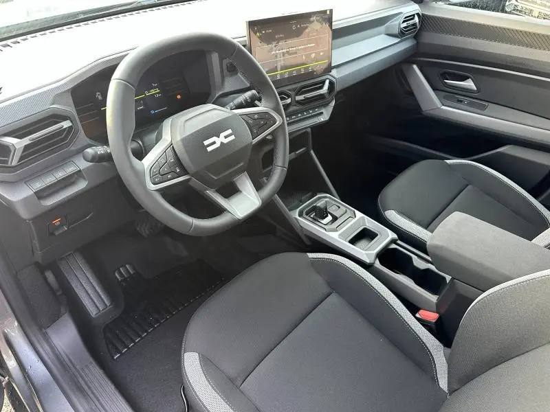 Vue intérieure côté conducteur du Dacia Duster 2025 hybride, avec volant multifonction et écran tactile central.