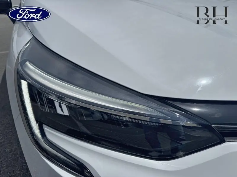Gros plan sur le phare avant gauche de la Renault Clio blanche 2023, soulignant son design LED moderne.