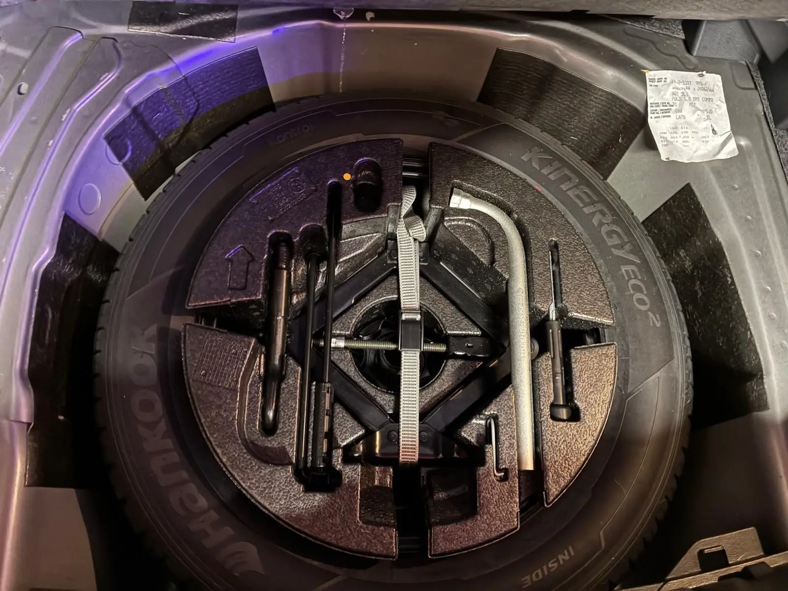 Vue plongeante sur la roue de secours et les outils de bord dans le coffre d'une Volkswagen Polo gris 2018.