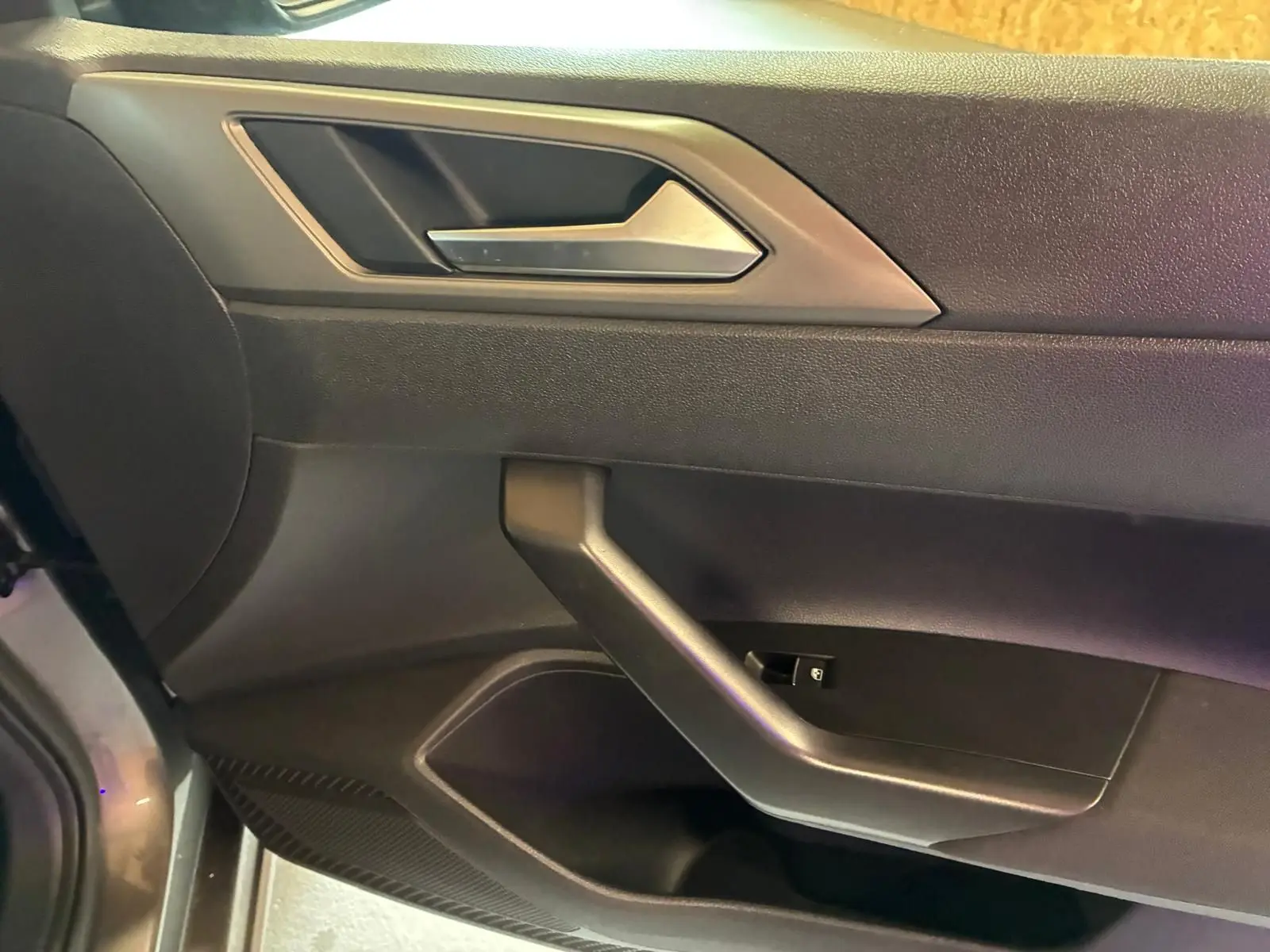Vue rapprochée de la porte intérieure côté gauche d'une Volkswagen Polo gris foncé avec poignée argentée et commandes de fenêtre.