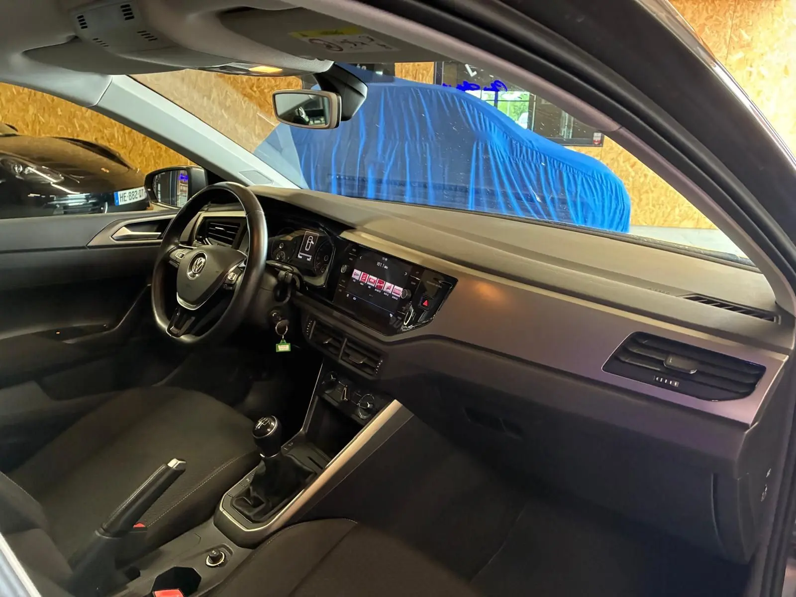 Vue intérieure côté conducteur de la Volkswagen Polo gris 2018, montrant le tableau de bord et la boîte manuelle.