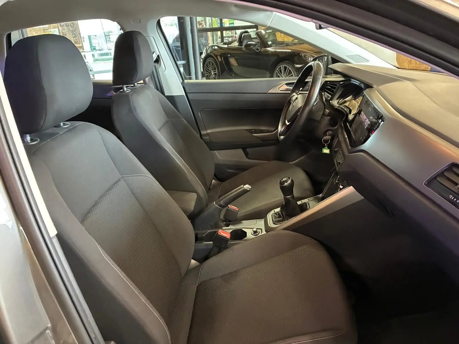 Vue intérieure côté conducteur de la Volkswagen Polo gris 2018, montrant les sièges tissu noirs et la boîte manuelle.