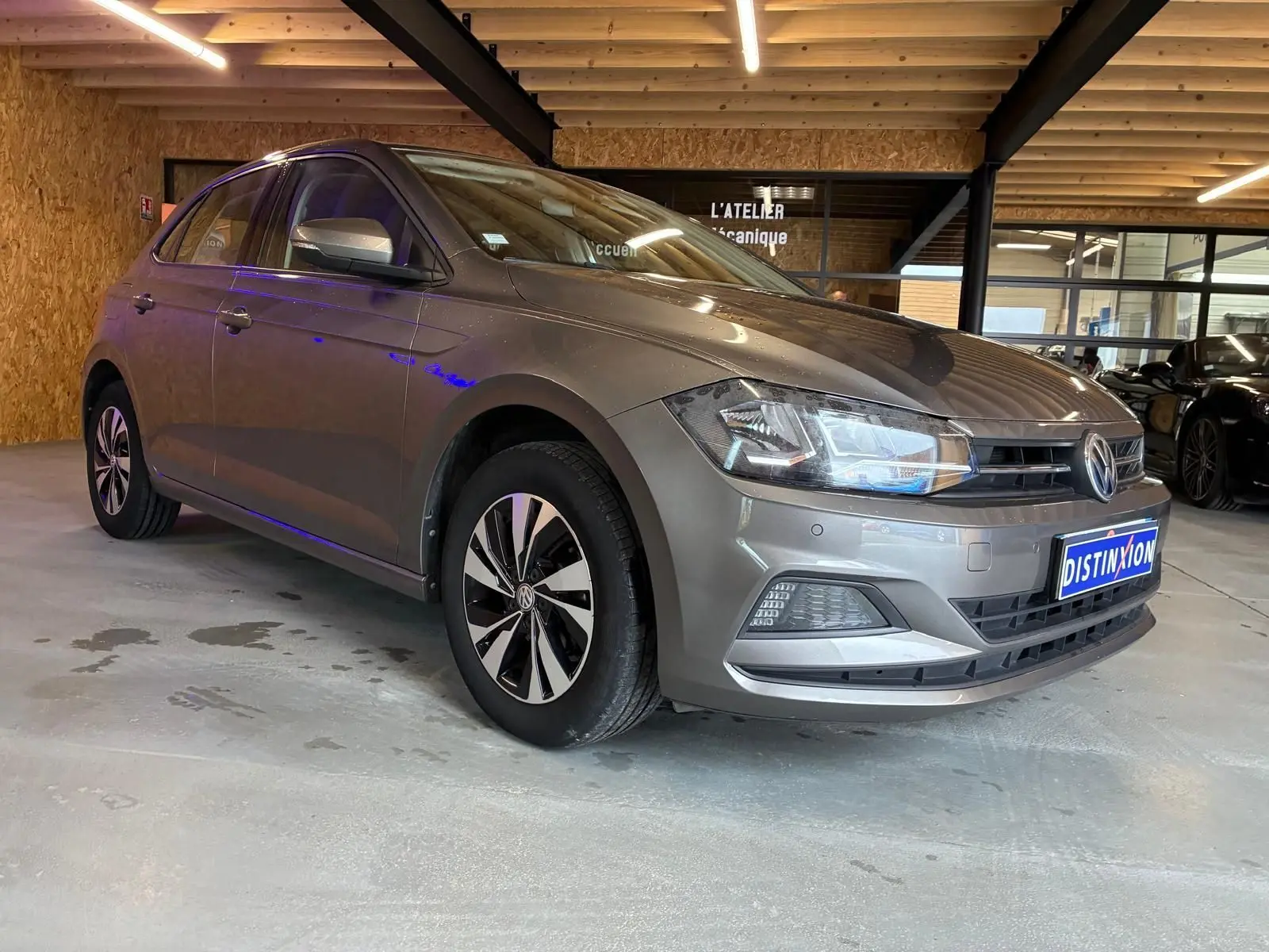 Volkswagen Polo gris 1.0 TSI 95 Confortline vue 3/4 avant droit dans un garage avec éclairage intérieur.