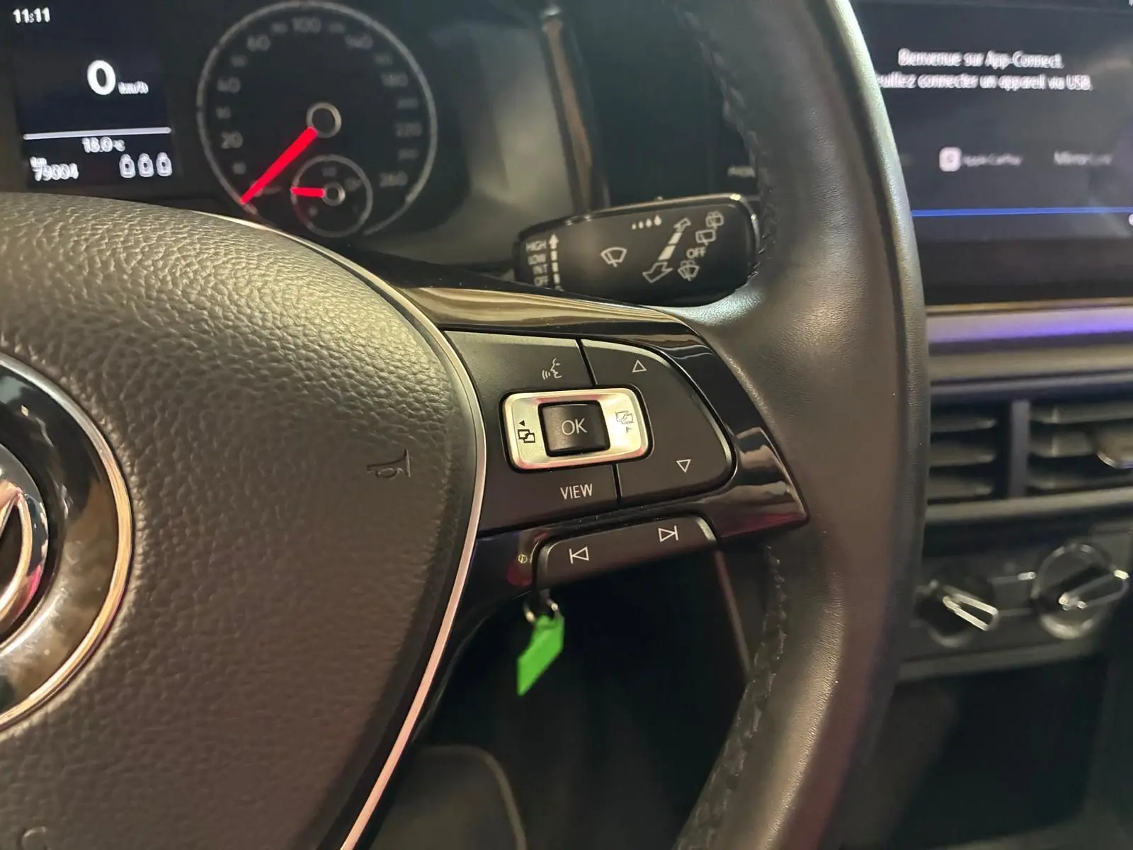 Gros plan sur le volant noir de la Volkswagen Polo 2018, avec commandes intégrées et tableau de bord numérique en arrière-plan.