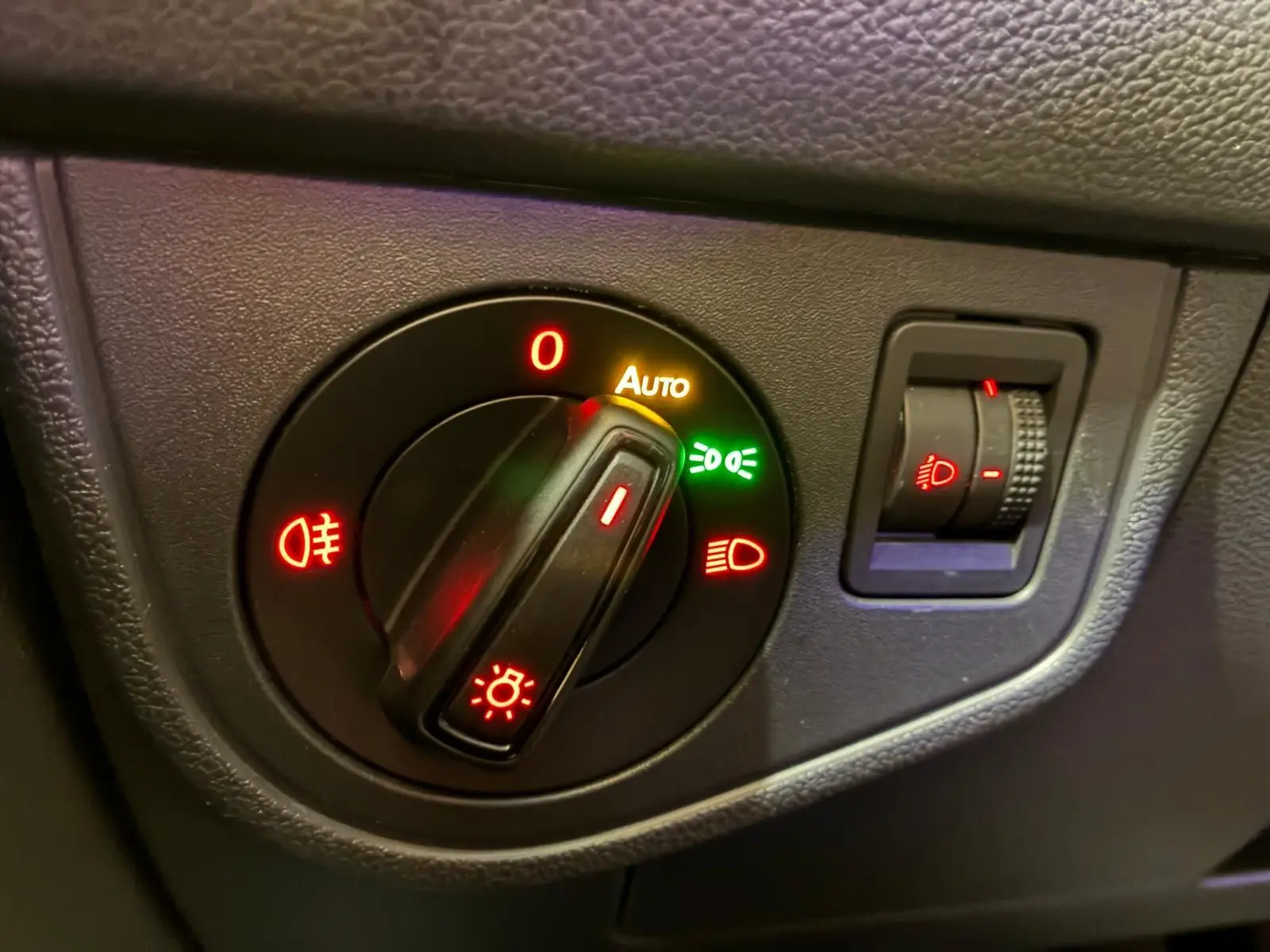 Gros plan sur le bouton de commande des phares avec réglage automatique, sur tableau de bord noir d'une Volkswagen Polo gris 2018.
