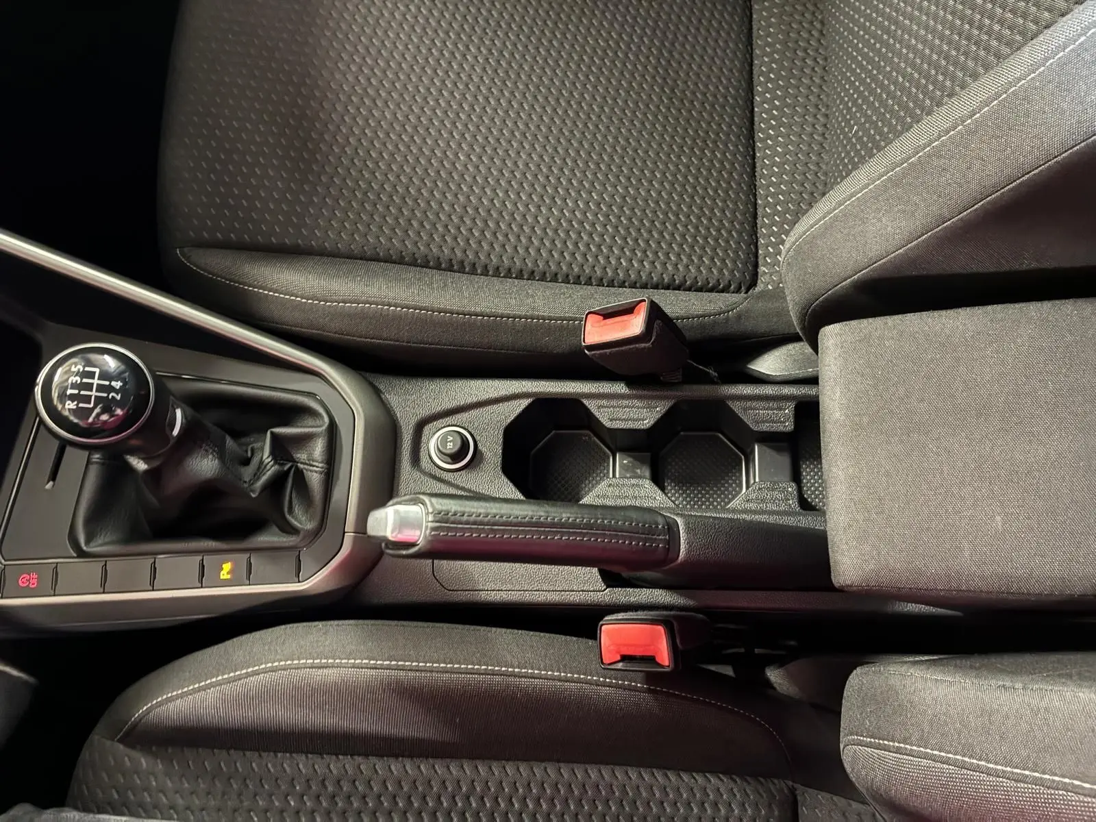 Vue rapprochée de la console centrale d’une Volkswagen Polo gris, montrant levier de vitesse manuel, frein à main et sièges en tissu noir.