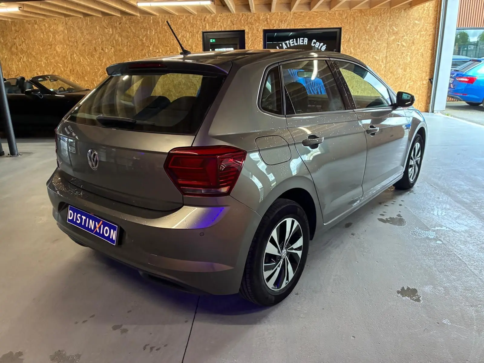 Volkswagen Polo gris vue 3/4 arrière droit dans un garage, avec jantes alliage et cinq portes visibles.