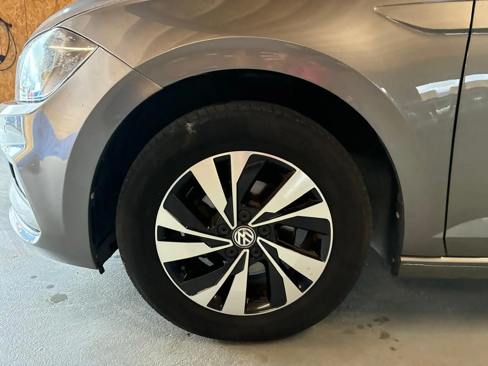 Gros plan sur la roue avant gauche d'une Volkswagen Polo gris métallisé avec jante noire et argentée au design moderne.