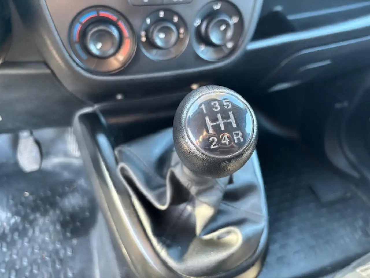 Gros plan sur le levier de vitesses manuel noir dans l’habitacle de l’Opel Combo blanc, avec commandes de climatisation en arrière-plan.