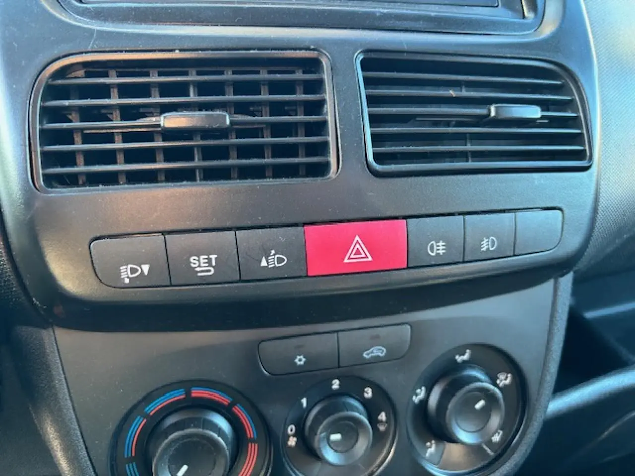 Détail de la console centrale de l’Opel Combo blanc 2015, montrant les commandes de climatisation et les boutons de sécurité.