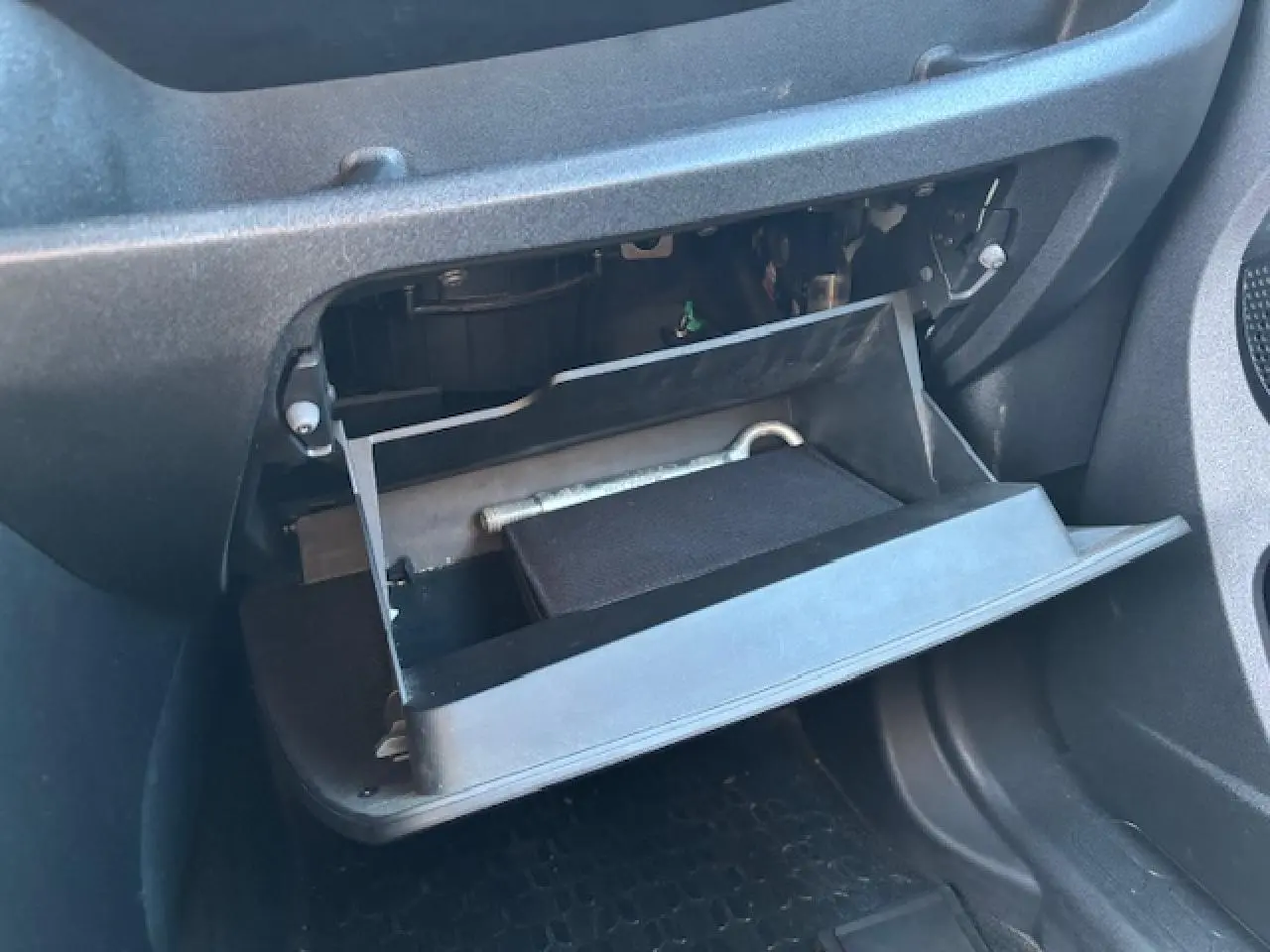 Gros plan sur la boîte à gants ouverte côté passager de l’Opel Combo blanc, montrant un outil et un carnet à l’intérieur.