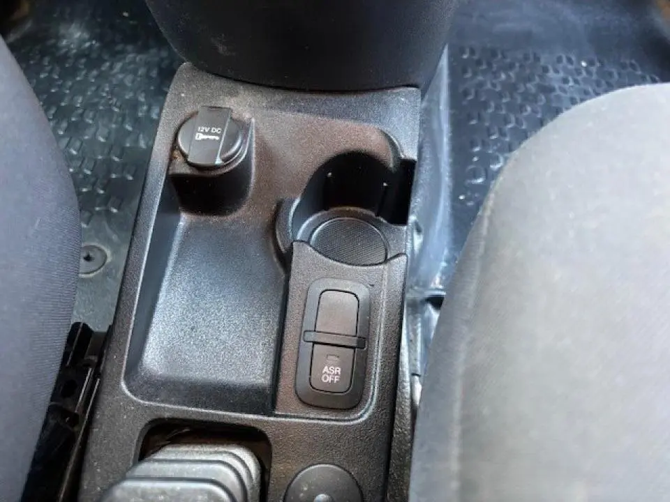 Détail de la console centrale noire de l'Opel Combo L1H1 2015 avec bouton ASR off et prise 12V visible entre les sièges.