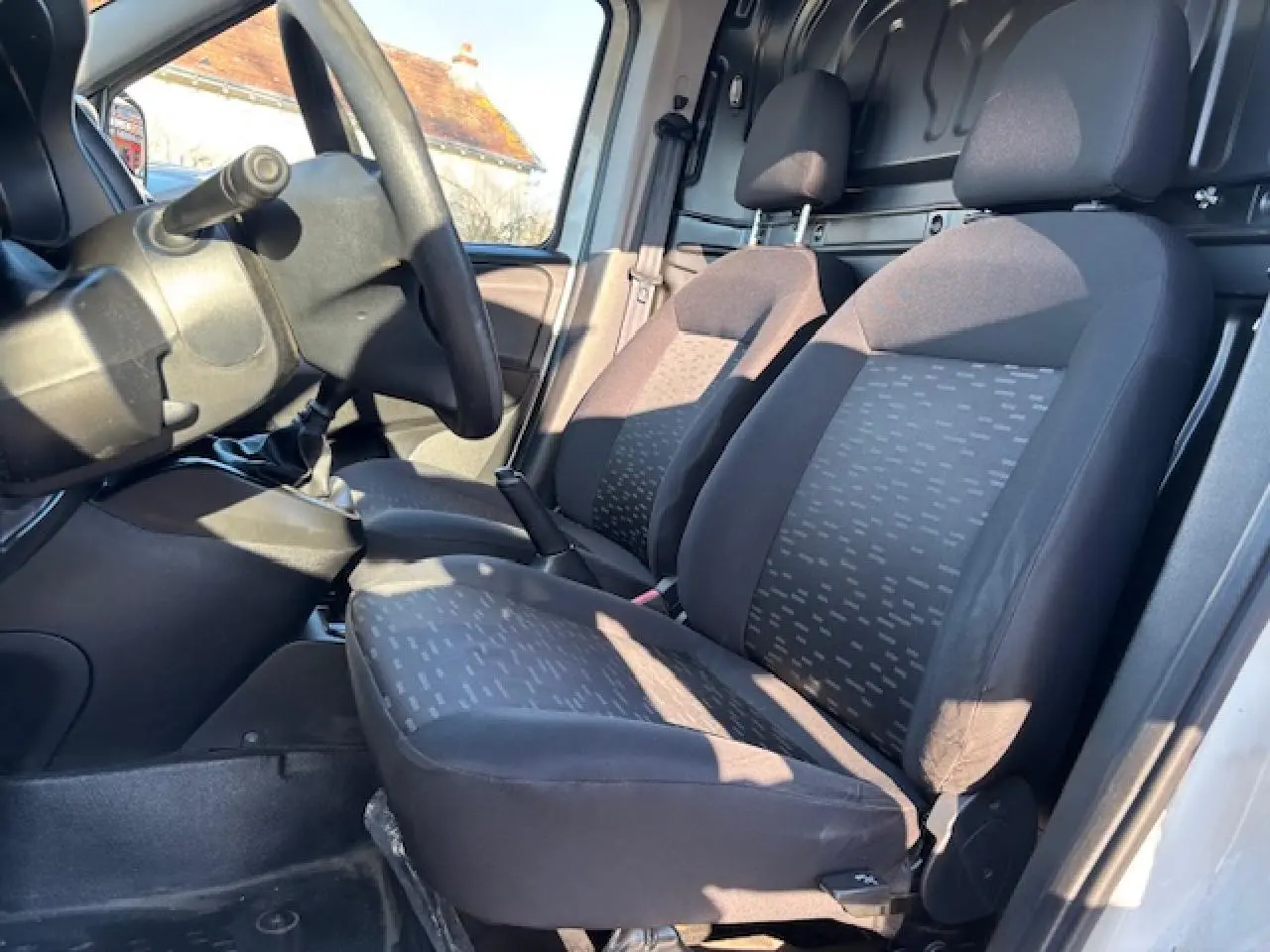 Vue intérieure côté conducteur de l’Opel Combo L1H1 2015, montrant les sièges avant en tissu gris et la cloison tôlée arrière.