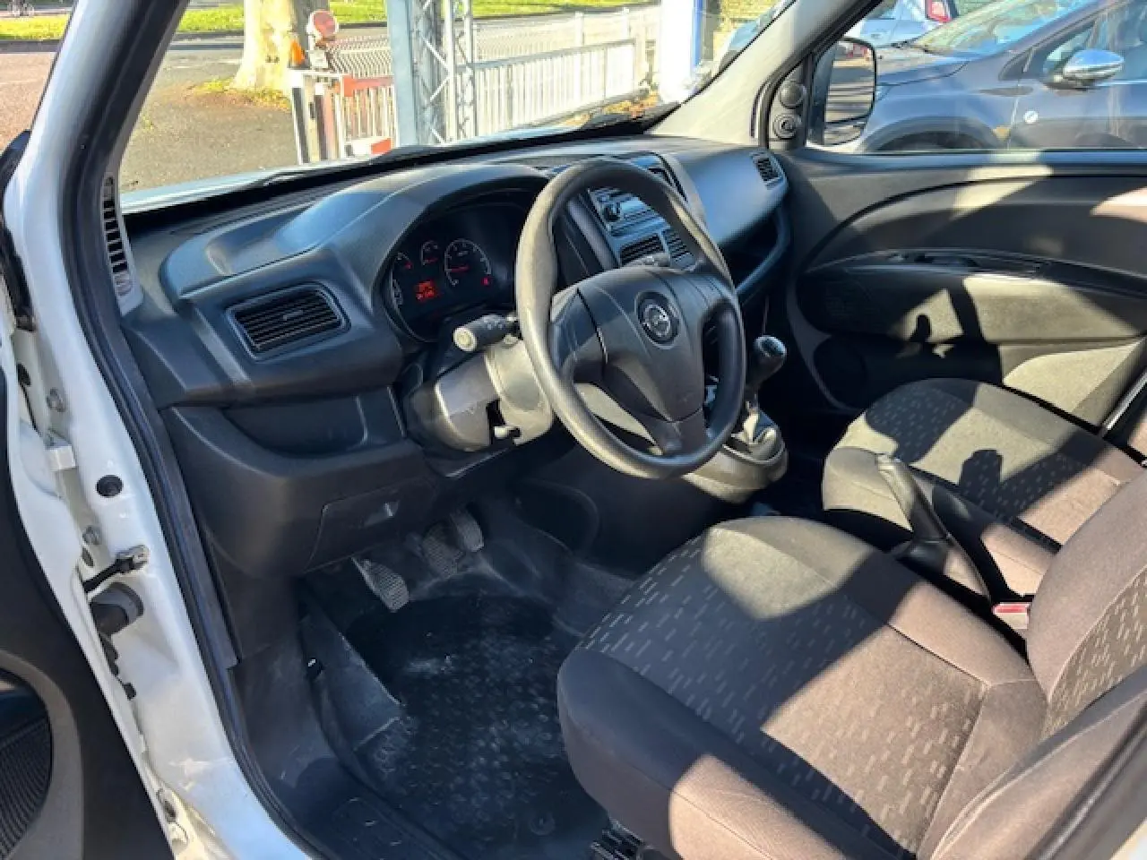 Vue intérieure côté conducteur de l'Opel Combo blanc, montrant le volant, tableau de bord et sièges avant en tissu noir.