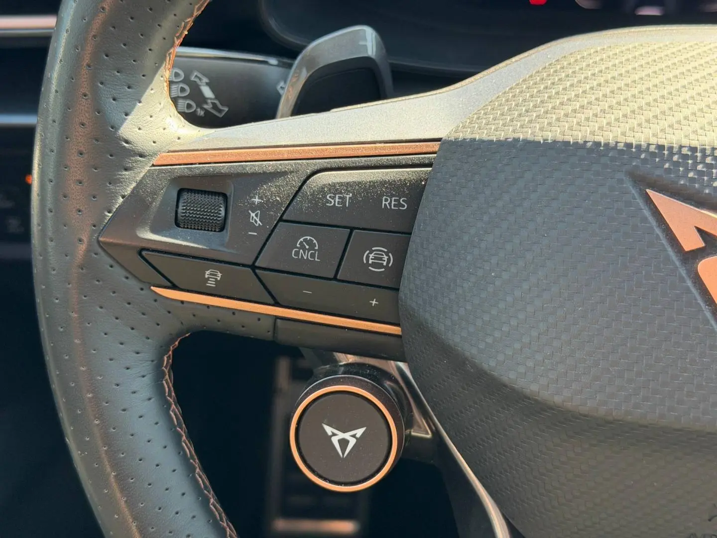 Gros plan sur le volant cuir perforé côté gauche du CUPRA Formentor gris métallisé avec commandes multifonctions et logo central cuivré.