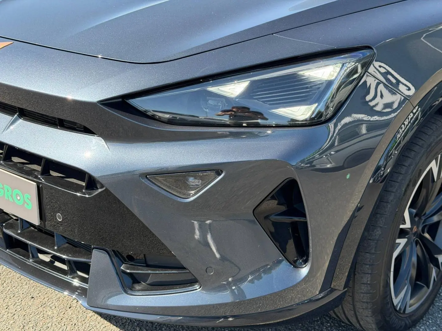 Gros plan sur l'avant droit du CUPRA Formentor gris magnétique métallisé, mettant en valeur le phare LED et la calandre sportive.