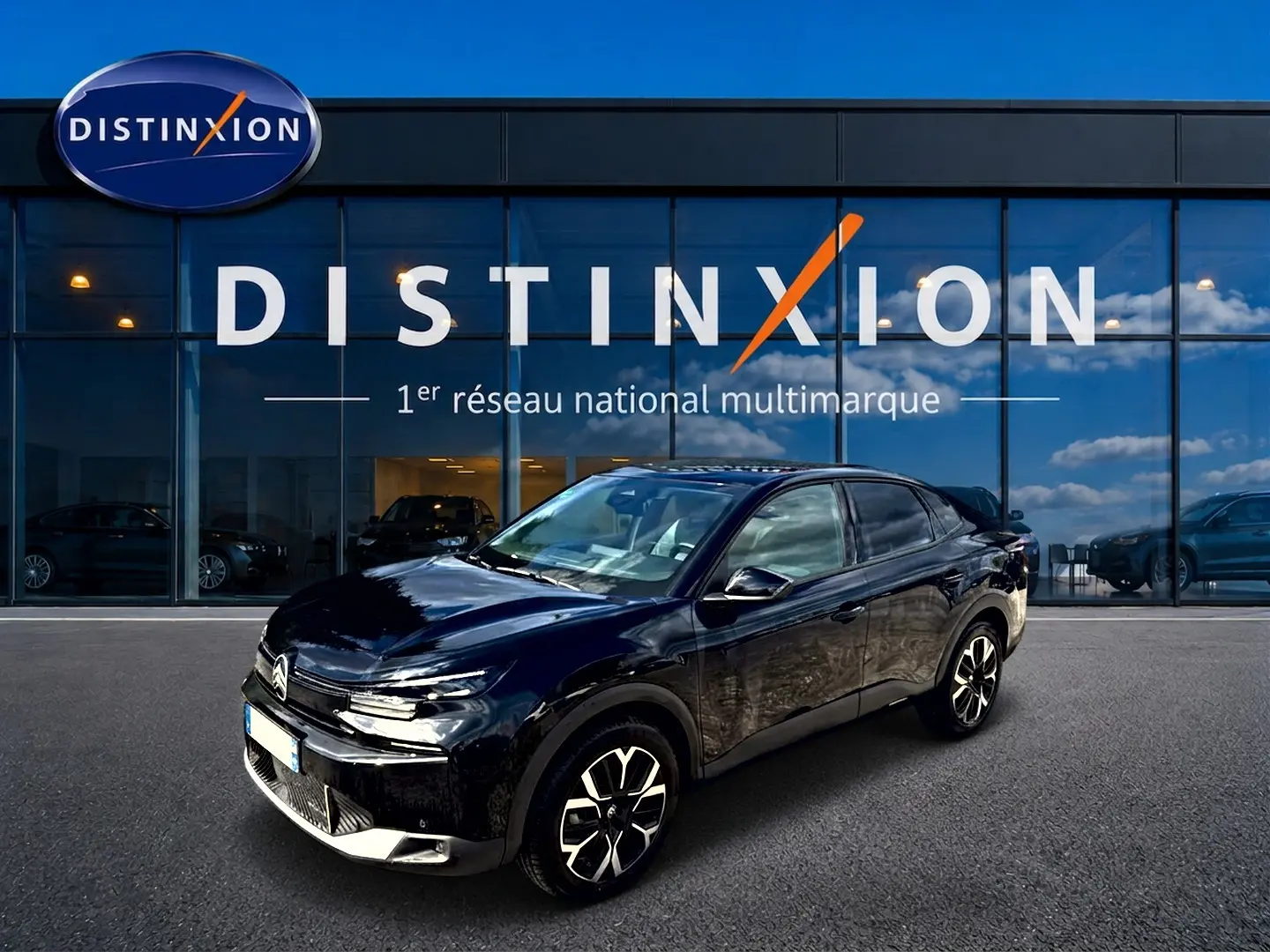 Vue 3/4 avant droite de la Citroën C4 X noire 2025 avec jantes alu et phares LED devant un showroom Distinxion.