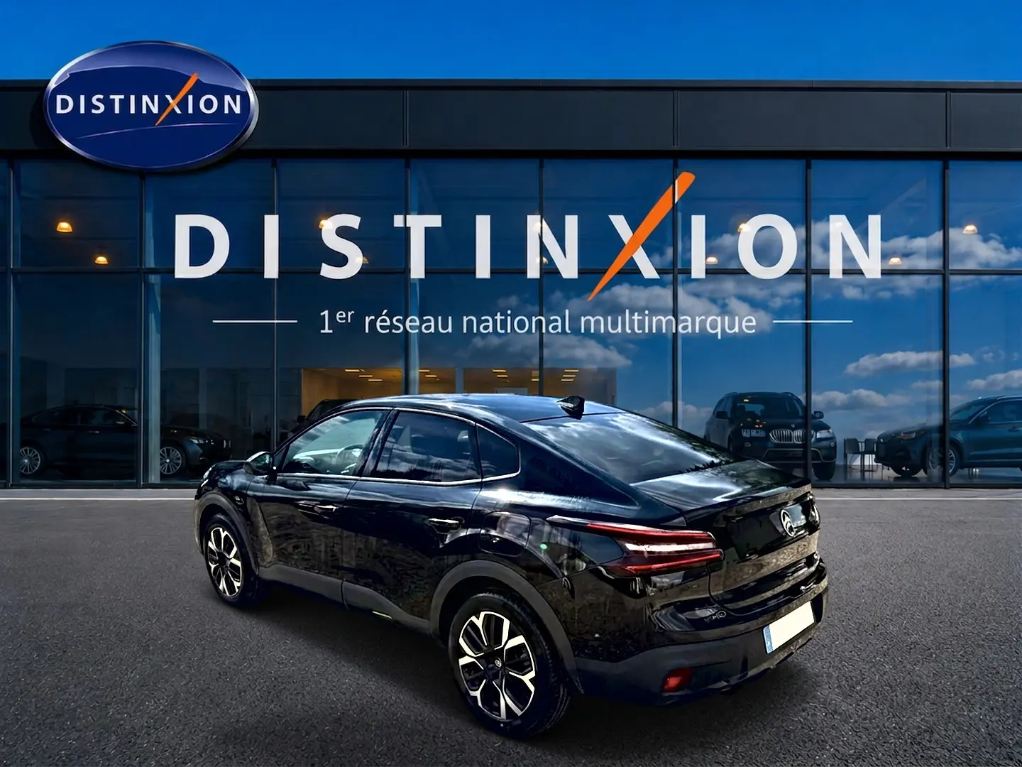 Vue 3/4 arrière droite d'une Citroën C4 X noire 2025 avec jantes alu et feux arrière LED, devant un showroom Distinxion.