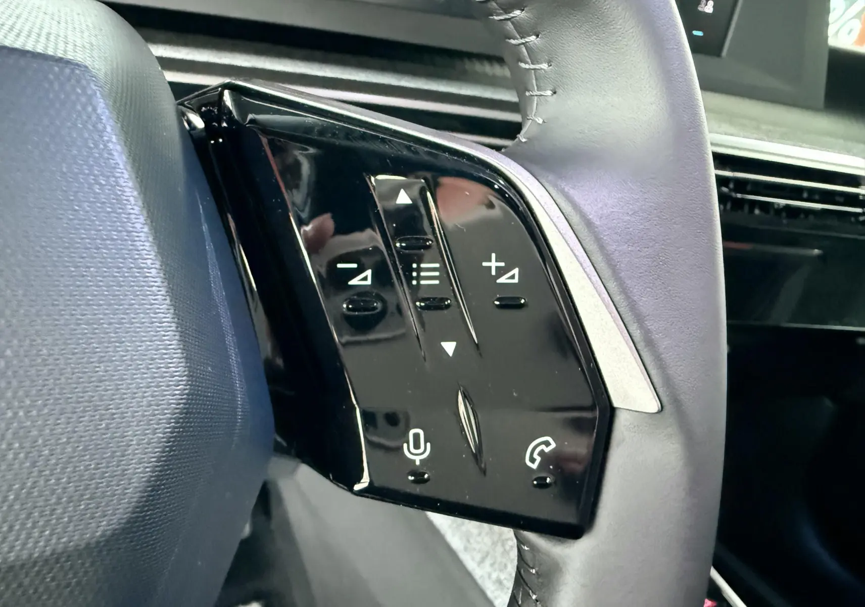 Gros plan sur les commandes au volant côté gauche du Peugeot 3008 Hybrid 2025 avec finition noire brillante.