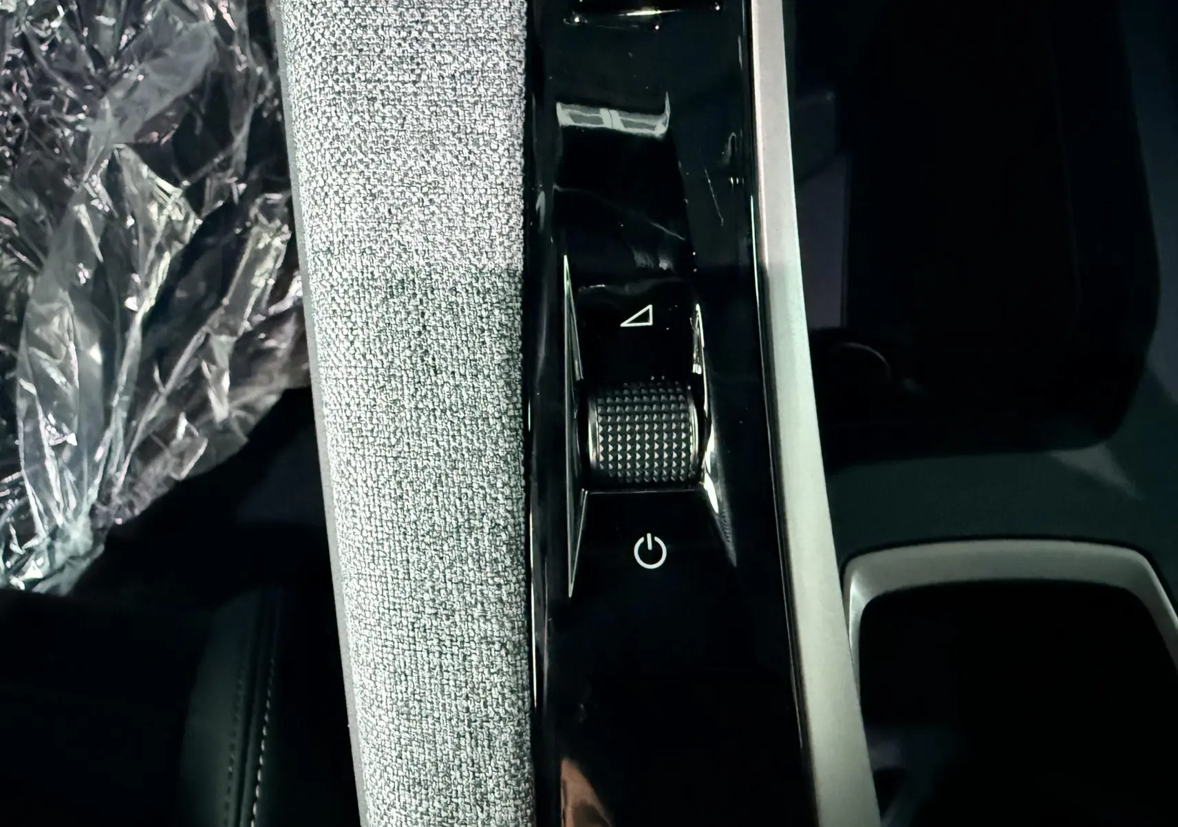 Gros plan sur la console centrale intérieure du Peugeot 3008 Hybrid 2025 avec molette de commande et tissu gris clair.