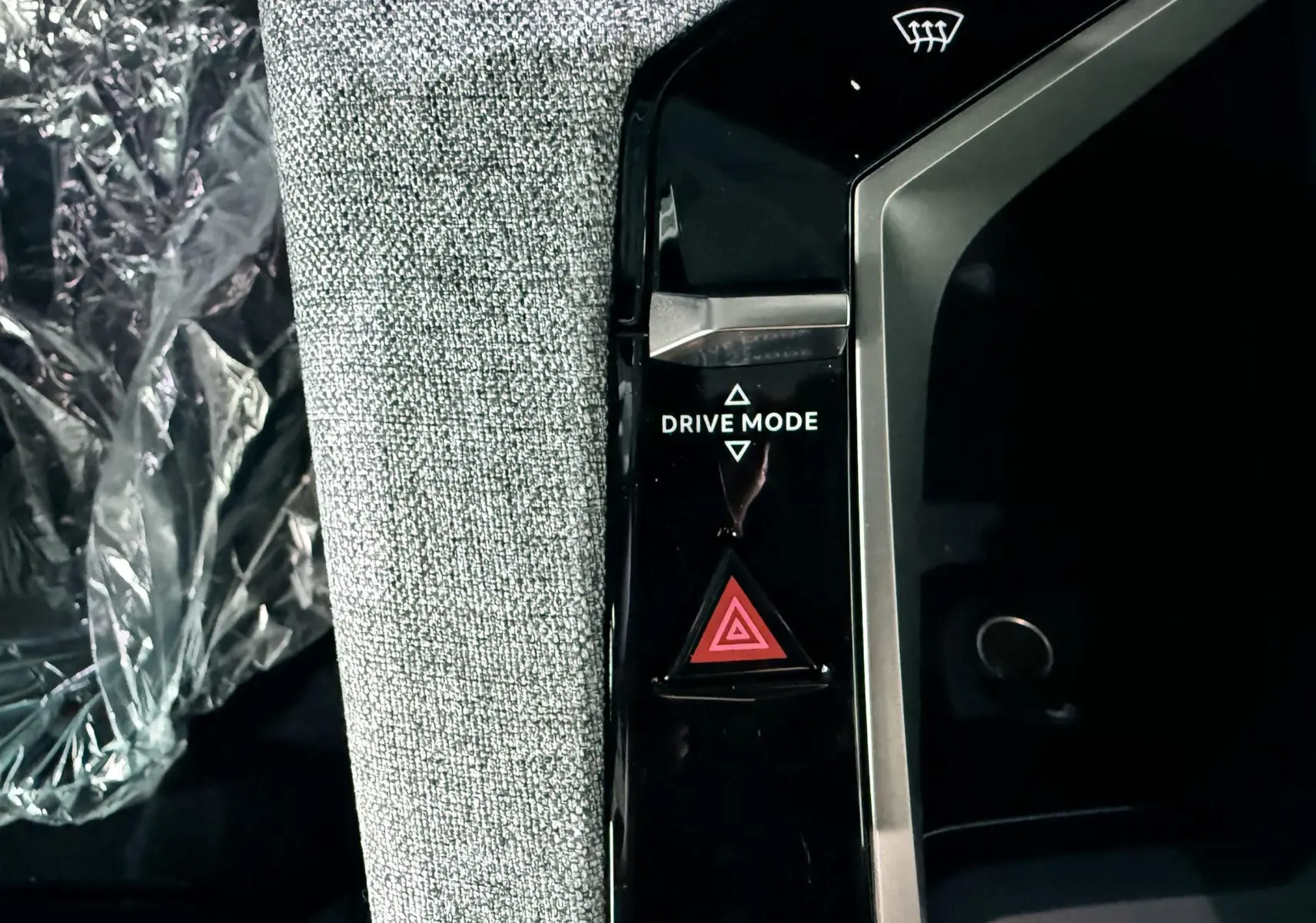 Gros plan sur la console centrale noire du Peugeot 3008 Hybrid 2025, avec bouton Drive Mode et alerte triangle rouge.