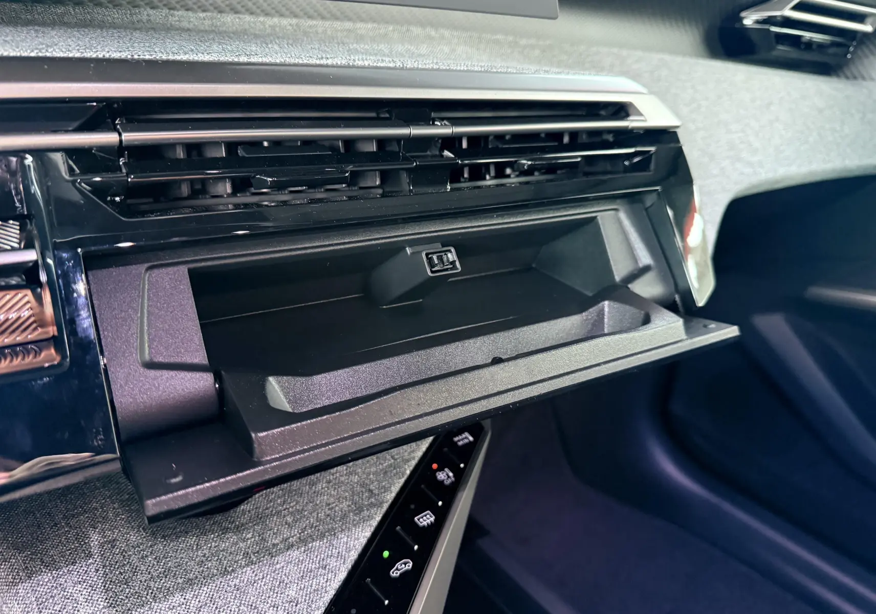 Gros plan sur la boîte à gants ouverte du Peugeot 3008 Hybrid 2025, avec tableau de bord noir et garniture grise.