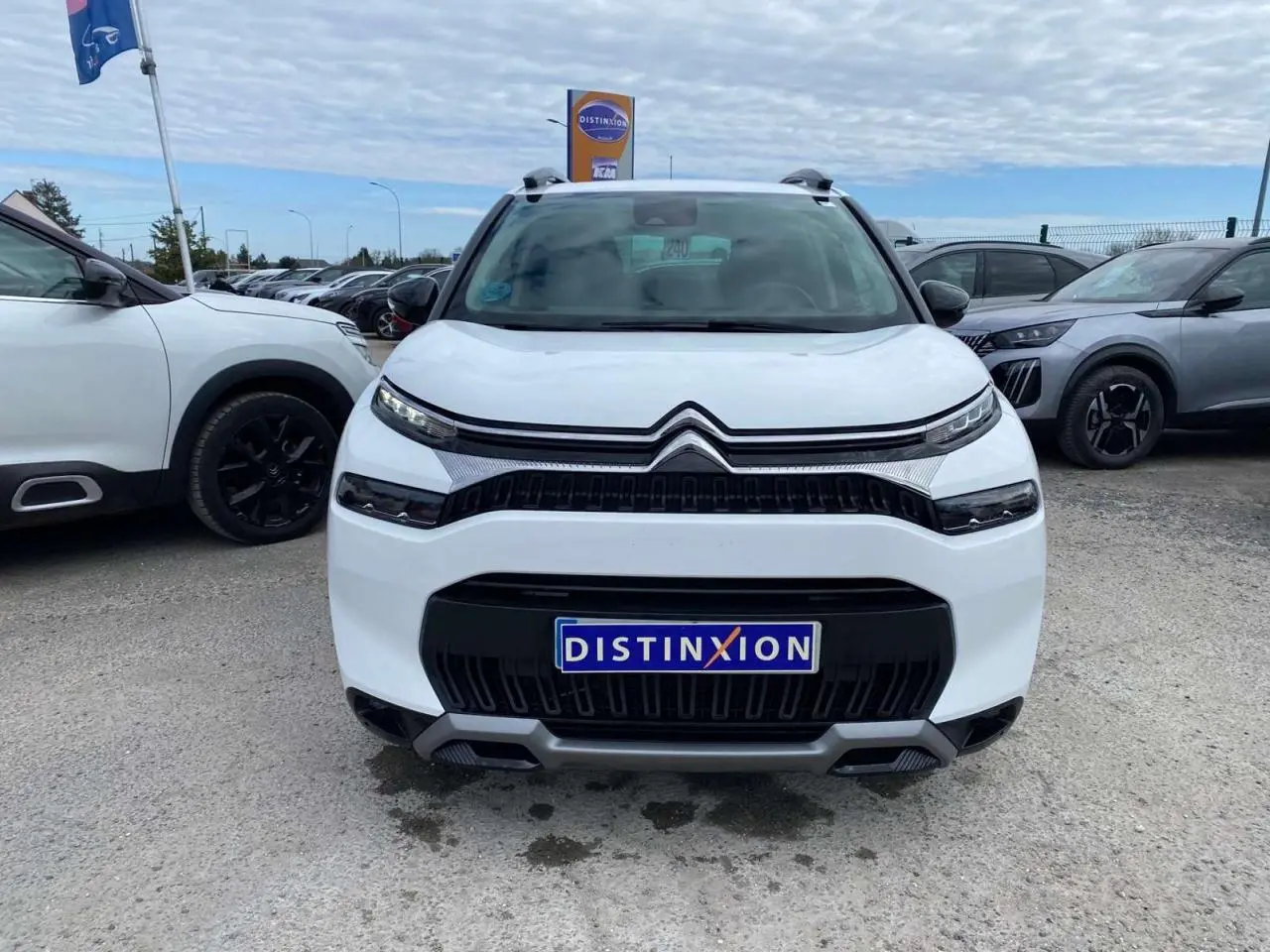 Vue avant d'un Citroën C3 Aircross blanc 2023 avec calandre noire et détails gris, sur parking extérieur.