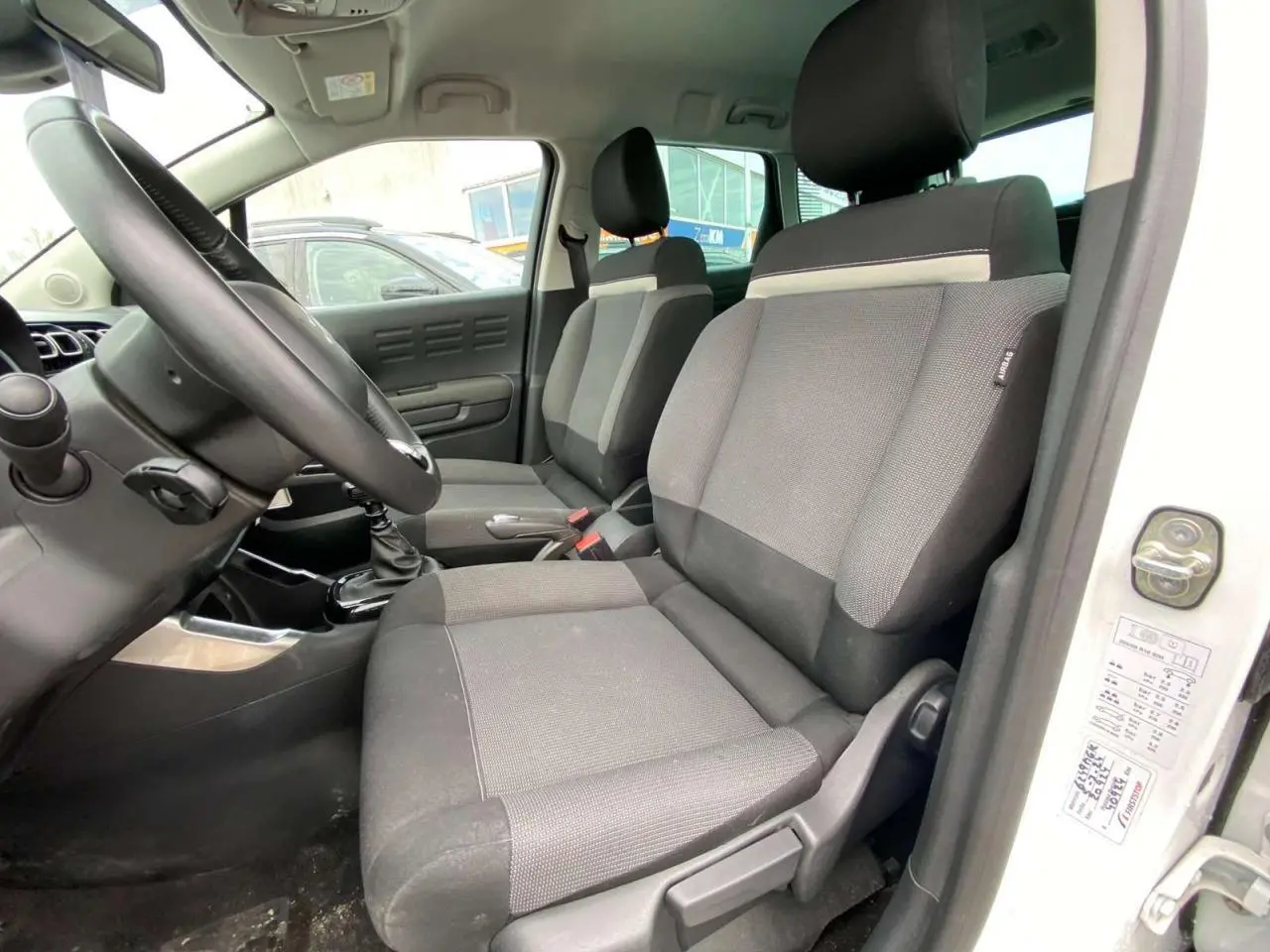 Vue intérieure côté conducteur du Citroën C3 Aircross blanc 2023, montrant les sièges avant en tissu gris et la boîte manuelle.
