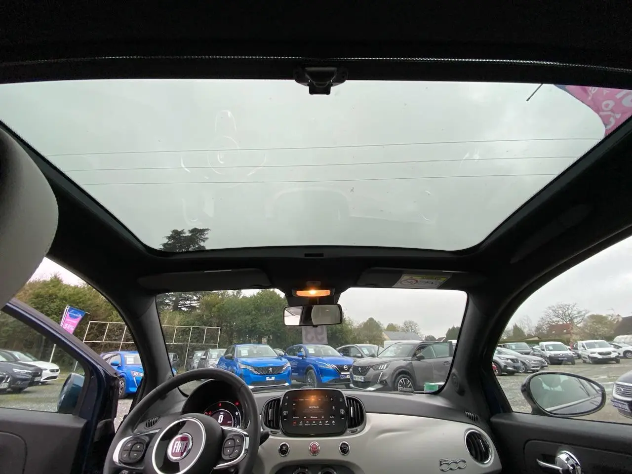 Vue intérieure du toit panoramique et du tableau de bord de la Fiat 500 2019, avec volant noir et tableau de bord clair.