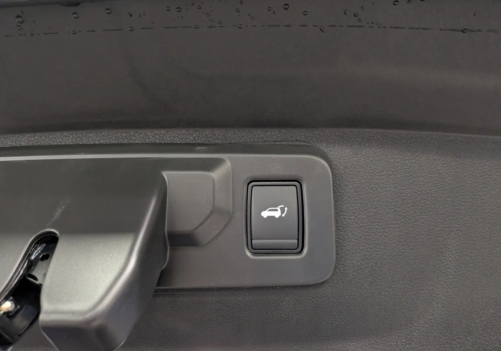 Bouton d'ouverture électrique du hayon sur la garniture intérieure du coffre d'une Renault Rafale gris schiste.