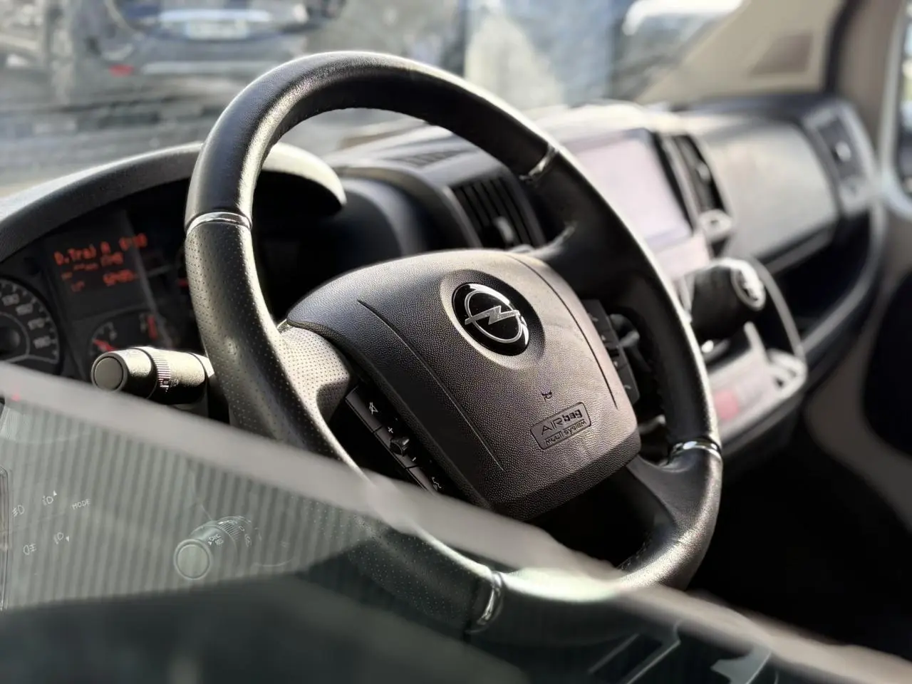 Intérieur de l'Opel Movano Fourgon 2024, vue rapprochée du volant noir avec logo Opel et tableau de bord flou.