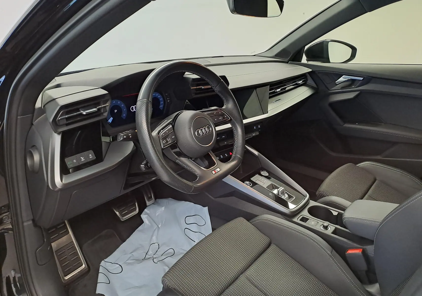 Vue intérieure côté conducteur de l'Audi A3 Sportback 35 TFSI 2023 en Noir Mythic, avec volant multifonction et tableau de bord digital.