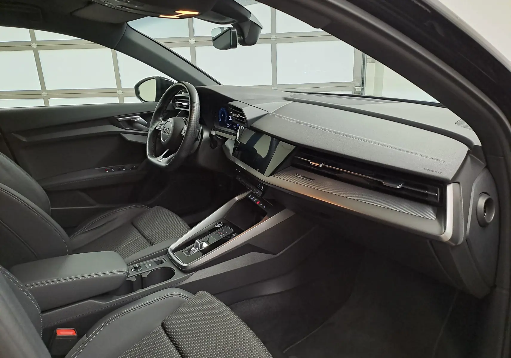 Vue intérieure côté conducteur de l'Audi A3 Sportback 35 TFSI S Line 2023 en Noir Mythic, avec tableau de bord moderne et écran tactile.