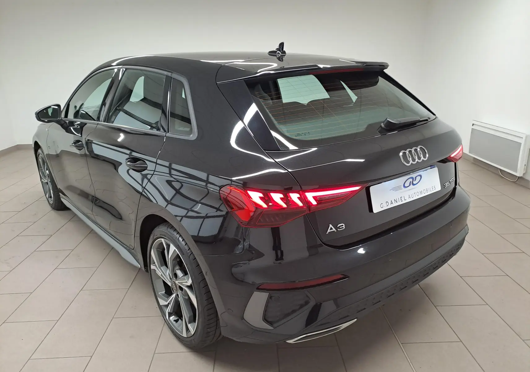 Audi A3 Sportback 35 TFSI S Line noir mythic vue 3/4 arrière droit avec feux LED allumés en intérieur.