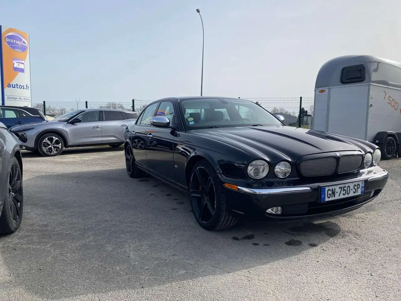 Jaguar XJ noire vue en 3/4 avant droit, avec calandre distinctive et jantes noires brillantes.