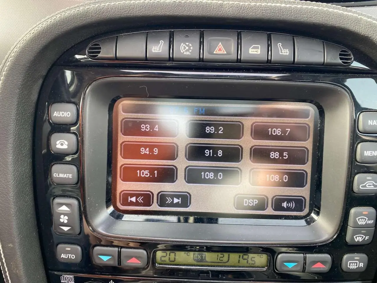 Gros plan sur le centre multimédia tactile de la Jaguar XJ noire de 2006, affichant les réglages radio et climatisation.