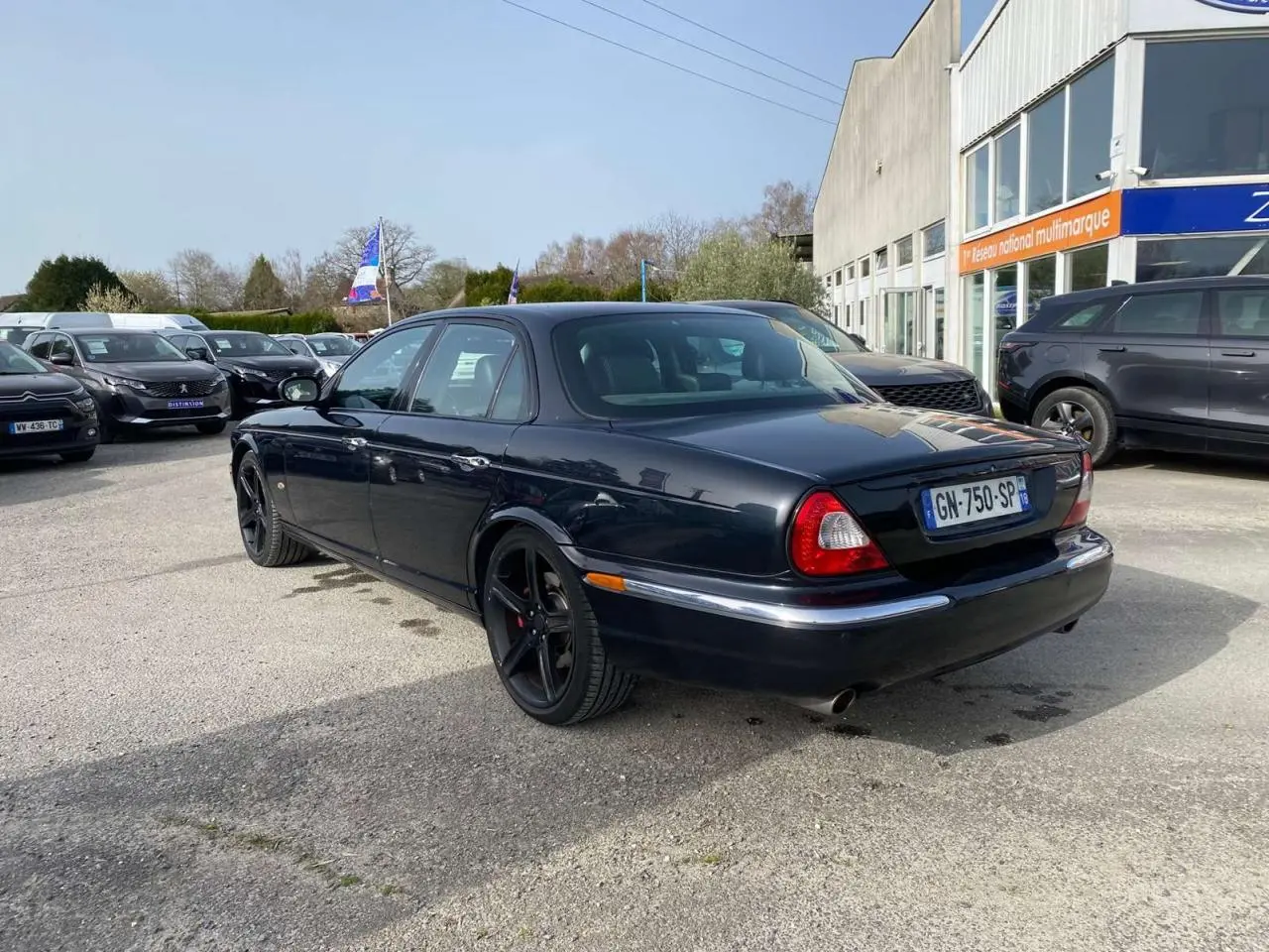 Jaguar XJ noir vue 3/4 arrière droit, avec jantes noires et feux arrière arrondis distinctifs.