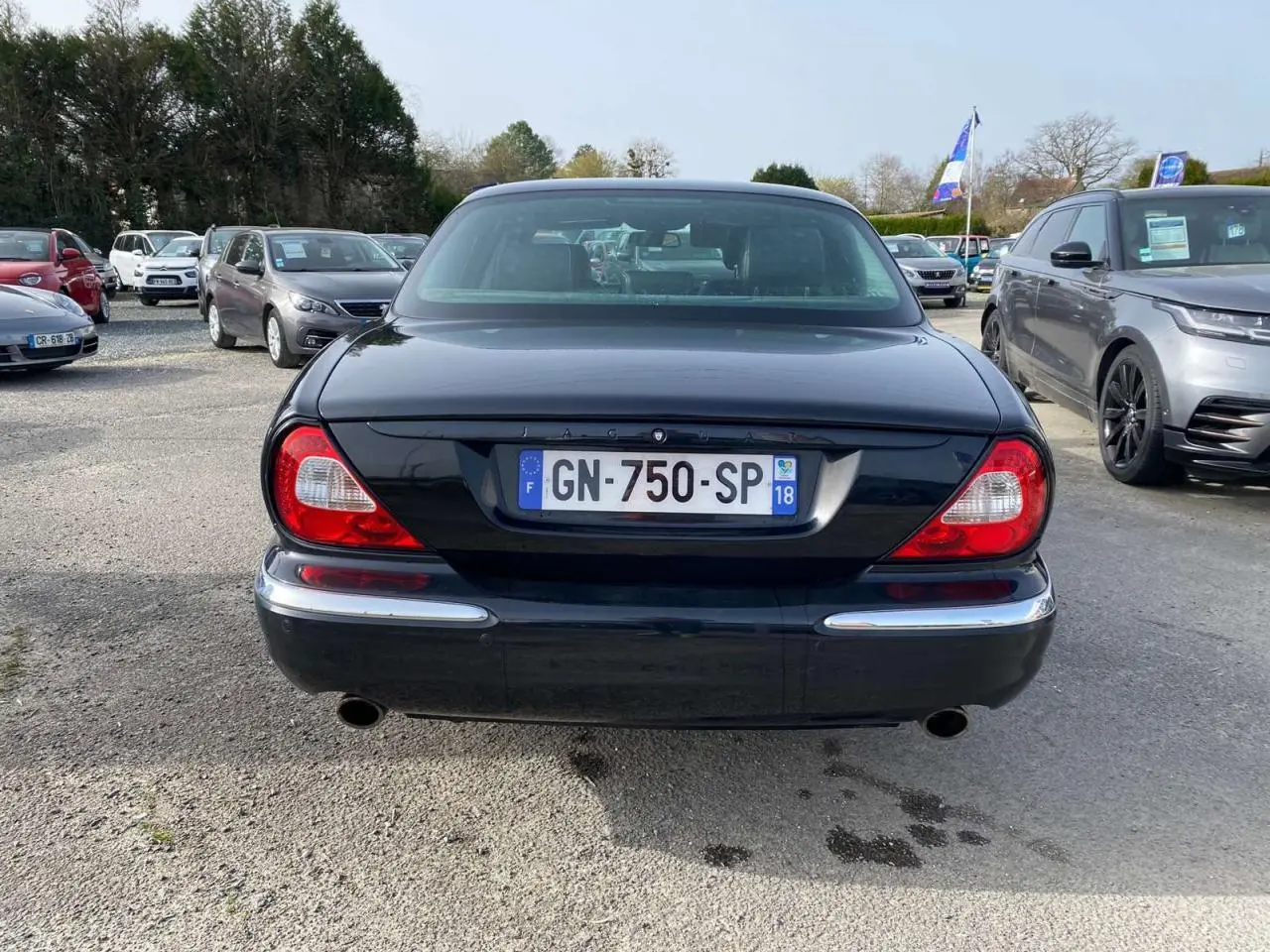 Vue arrière d'une Jaguar XJ noire de 2006, avec feux rouges caractéristiques et double sortie d'échappement visible.