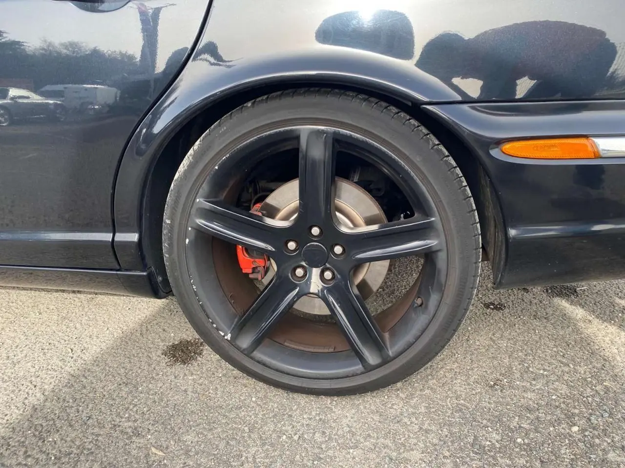 Gros plan sur la roue arrière droite noire d'une Jaguar XJ 2.7 V6 D Bi-TURBO 2006 avec étrier de frein rouge.