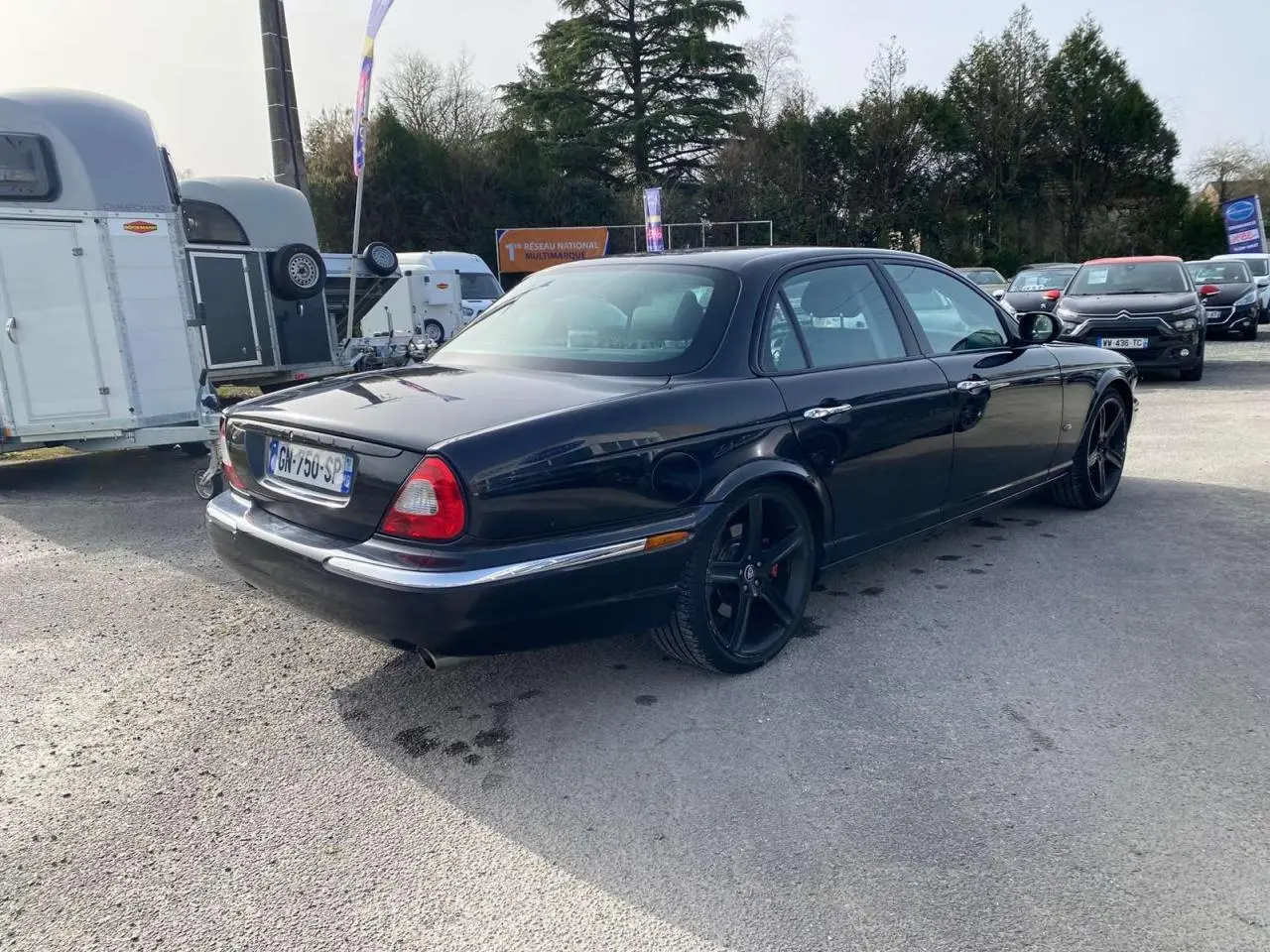 Jaguar XJ noire vue 3/4 arrière droit, avec jantes noires et feux arrière caractéristiques visibles.