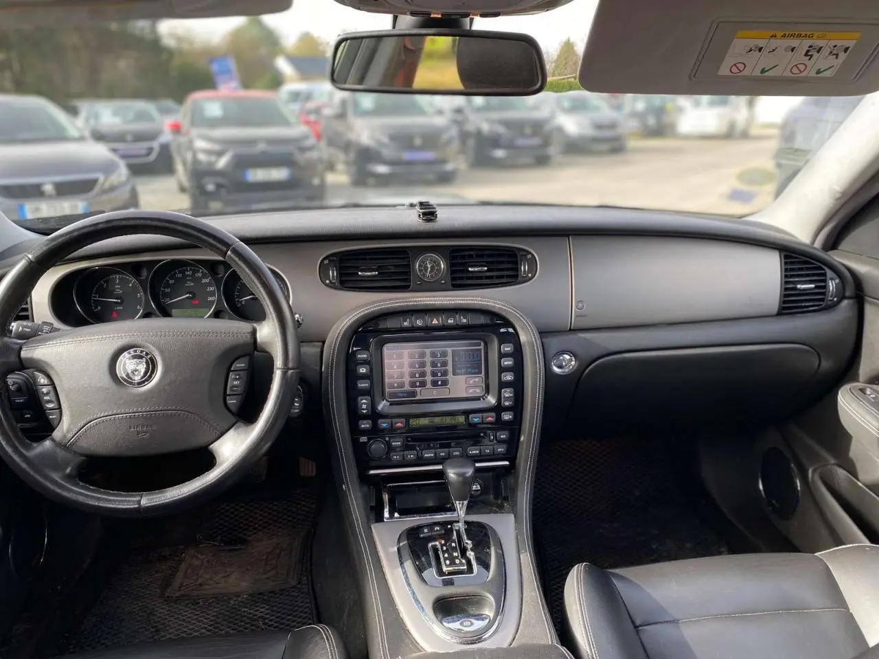 Vue intérieure avant de la Jaguar XJ 2006 noire, montrant le tableau de bord avec écran tactile central et volant cuir.
